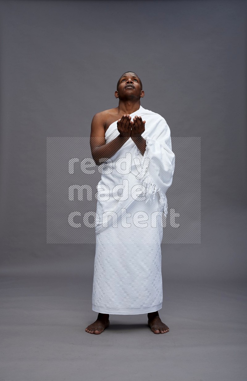 A man wearing Ehram Standing dua'a on gray background