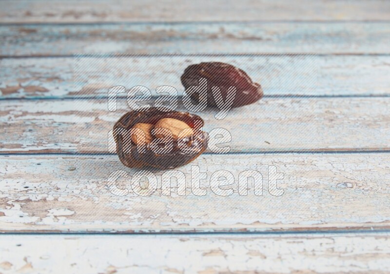 two almond stuffed madjoul dates on a light blue wooden background