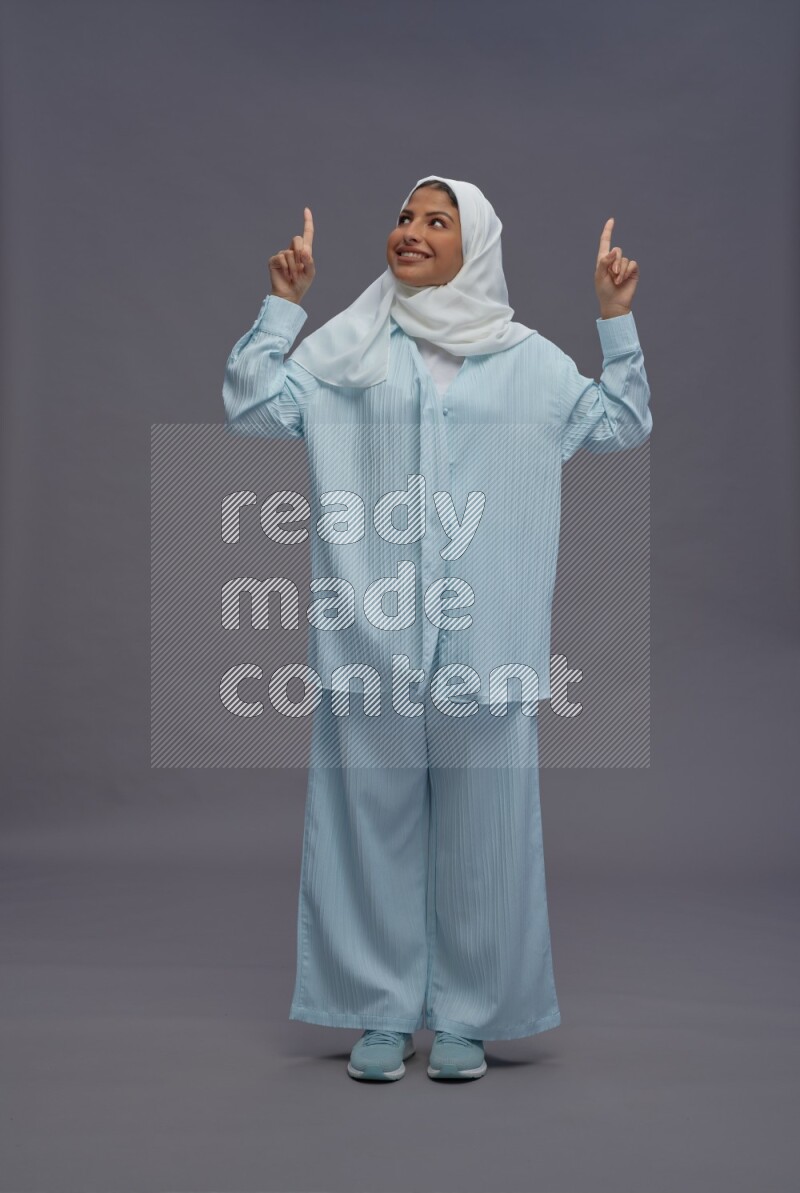 Saudi woman wearing hijab clothes standing interacting with the camera on gray background
