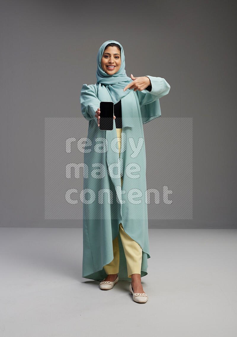 Saudi Woman wearing Abaya standing showing phone to camera on Gray background
