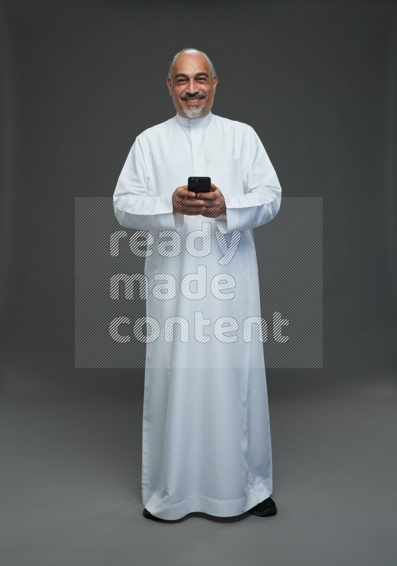 Saudi man without shomag Standing texting on phone on gray background