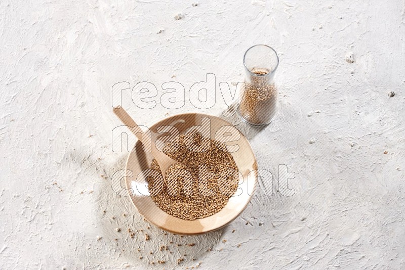 A multicolored pottery plate and a wooden spoon and a glass jar filled with mustard seeds on a textured white flooring in different angles
