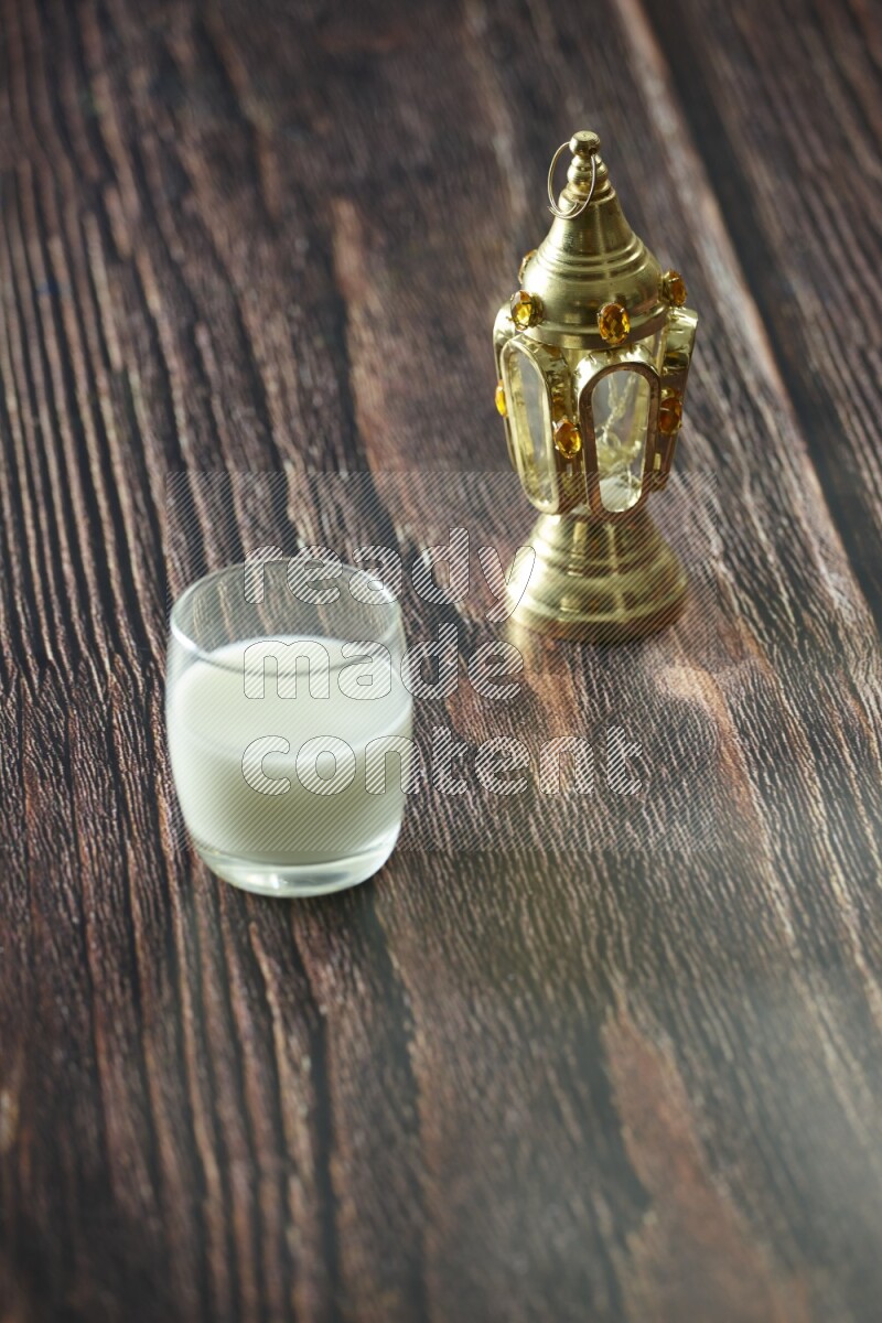 A golden lantern with different drinks, dates, nuts, prayer beads and quran on brown wooden background
