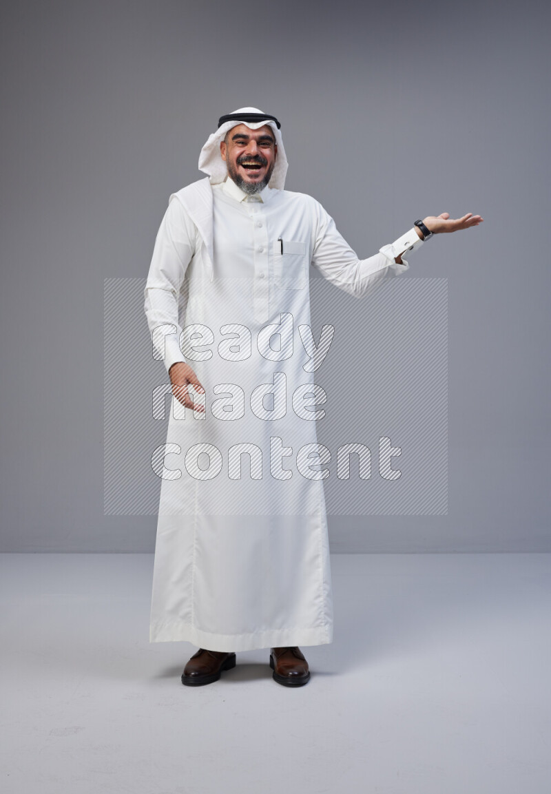 Saudi man Wearing Thob and white Shomag standing interacting with the camera on Gray background
