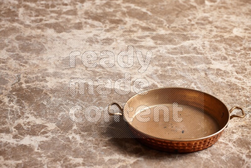 A small copper pan on beige marble background