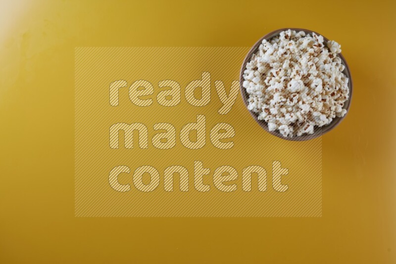 A brown pottery bowl full of popcorn on a yellow background in different angles