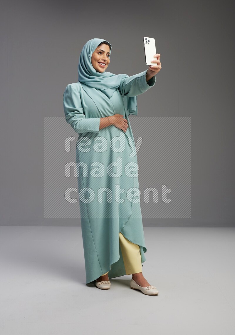 Saudi Woman wearing Abaya standing taking selfie on Gray background