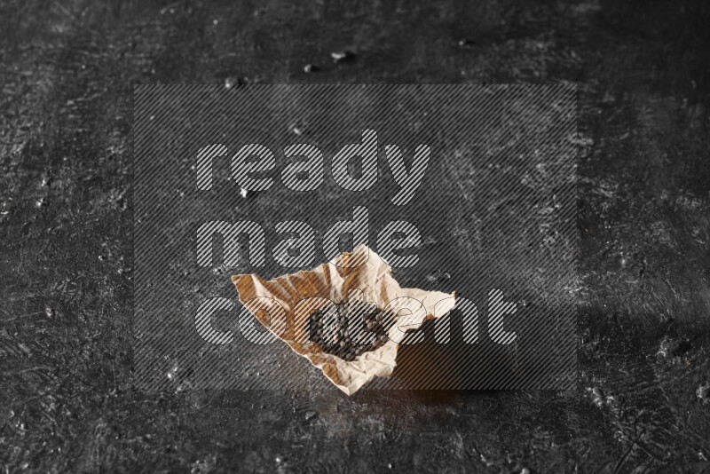 حبوب الفلفل الأسود في قطعة من الورق علي خلفية سوداء