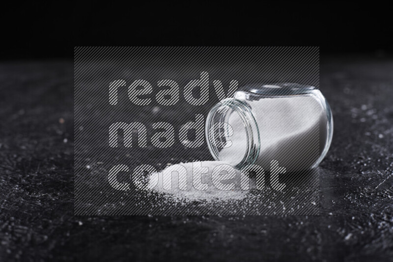 A glass jar full of fine table salt on black background