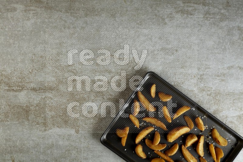 wedges potato in a black stainless steel rectangle tray on grey textured counter top