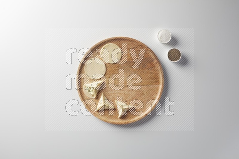 two closed sambosas and one open sambosa filled with cheese while salt, and black pepper aside in a wooden dish on a white background