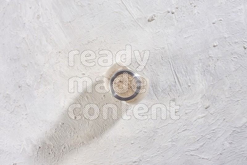 A glass spice jar full of garlic powder on a textured white flooring in different angles