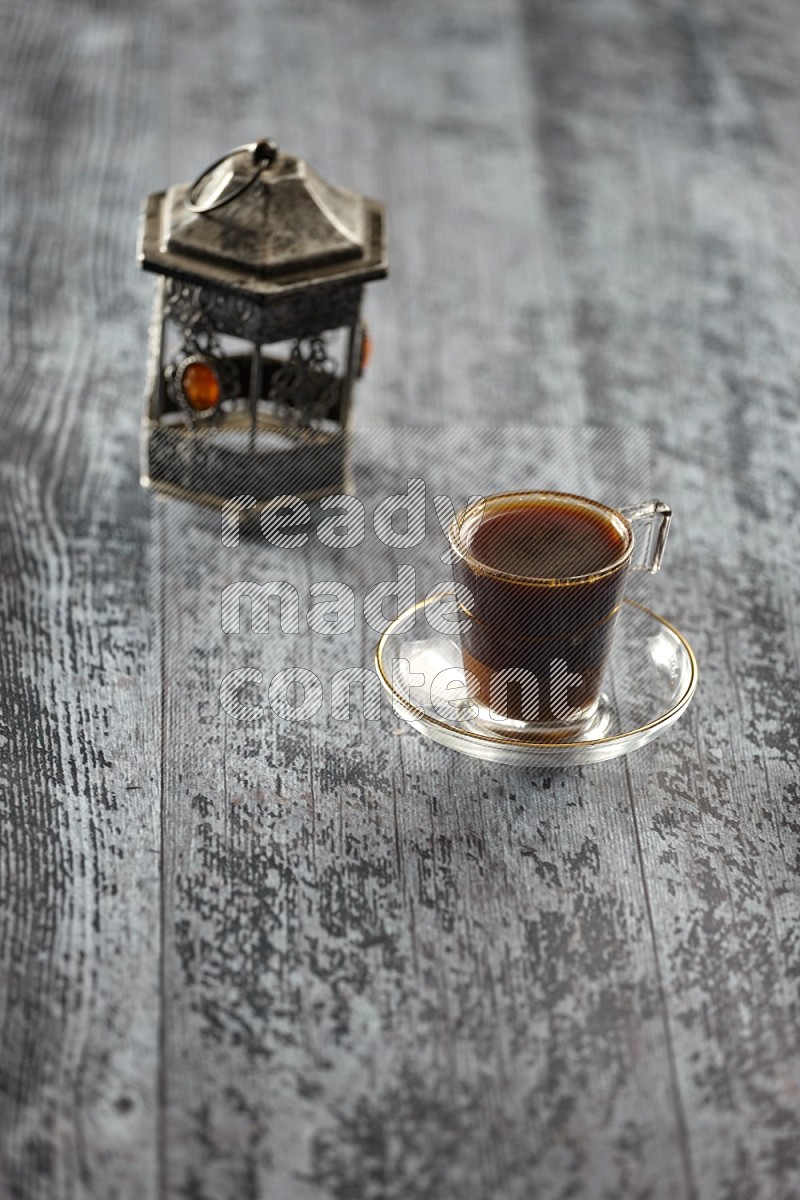 A silver lantern with different drinks, dates, nuts, prayer beads and quran on grey wooden background