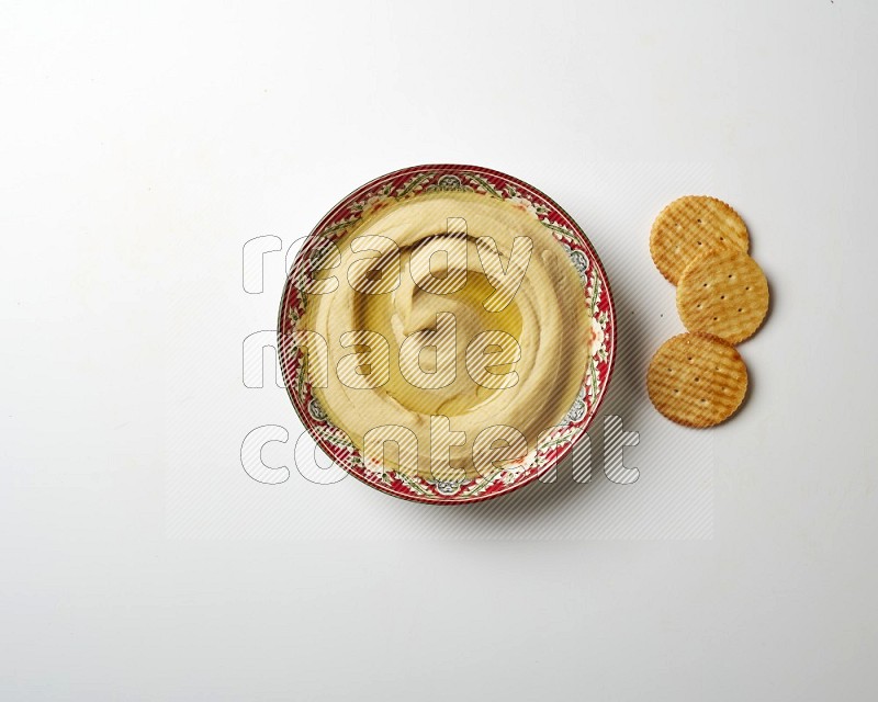 Hummus in a red plate with patterns garnished with olive oil on a white background