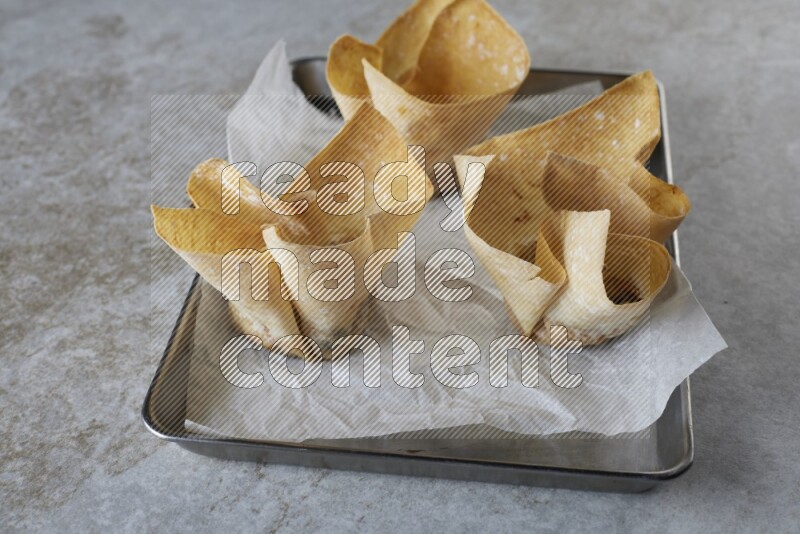 wonton cups on parchment paper in stainless tray on grey textured counter top