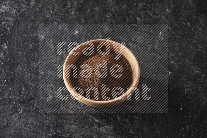 A wooden bowl full of cloves powder on a textured black flooring