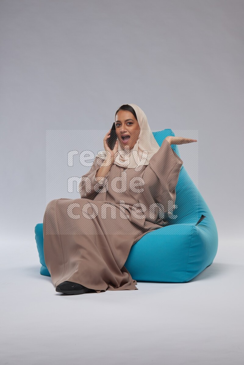 A Saudi woman sitting on a blue beanbag and working on laptop