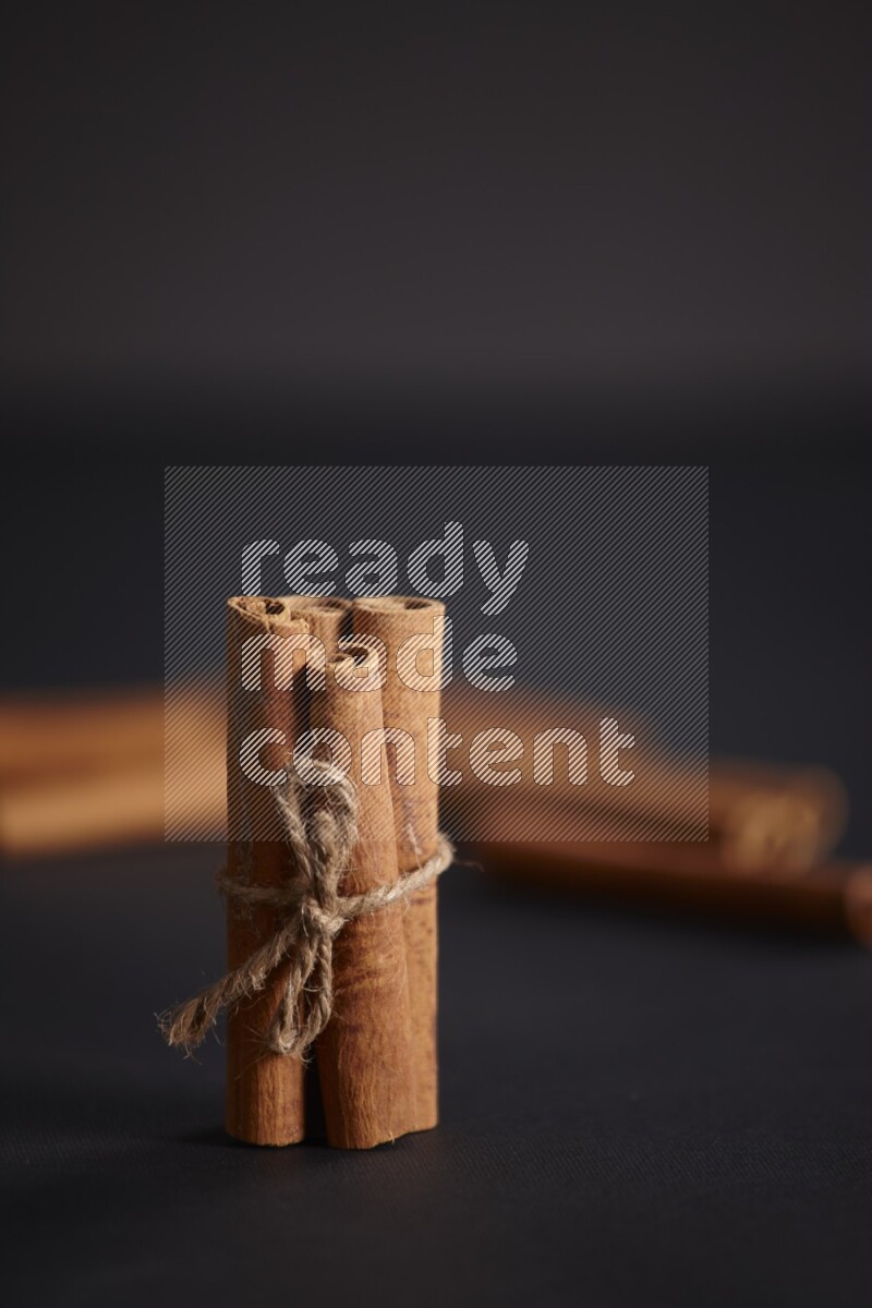 4 Cinnamon sticks stacked and bounded with more sticks in the background on black flooring