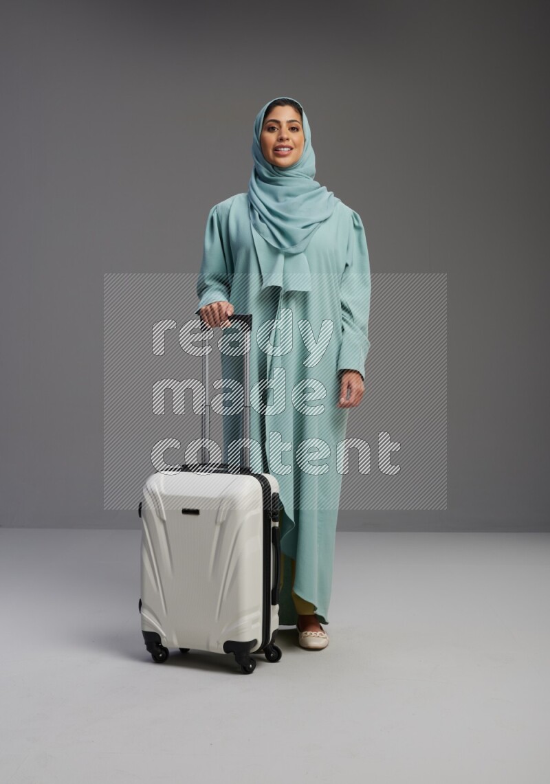 Saudi Woman wearing Abaya standing holding Travel bag on Gray background