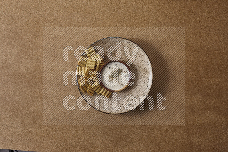 Assorted snacks on a pottery plate with a dipping on brown background