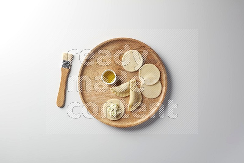two closed sambosas and one open sambosa filled with cheese while oil with oil brush aside in a wooden dish on a white background