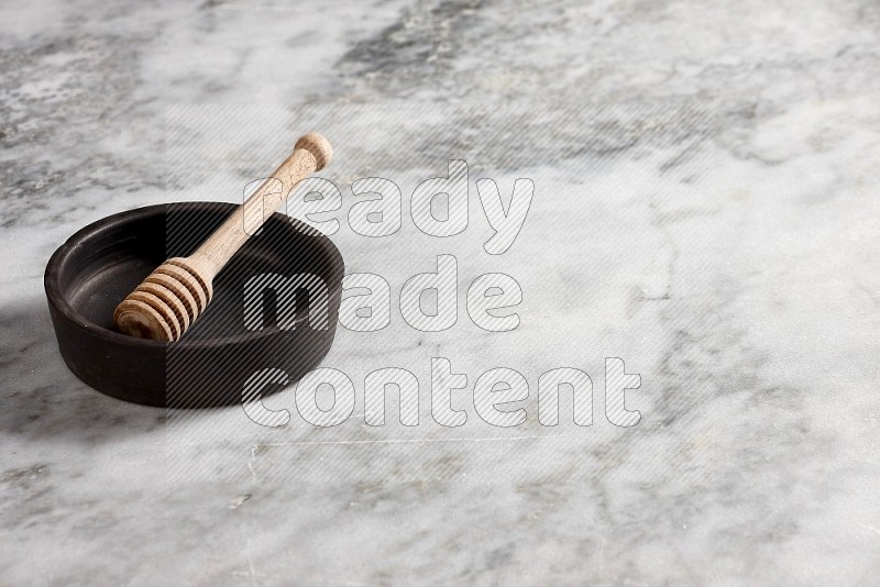 Black Pottery Oven Plate with wooden honey handle in it, on grey marble flooring, 45 degree angle