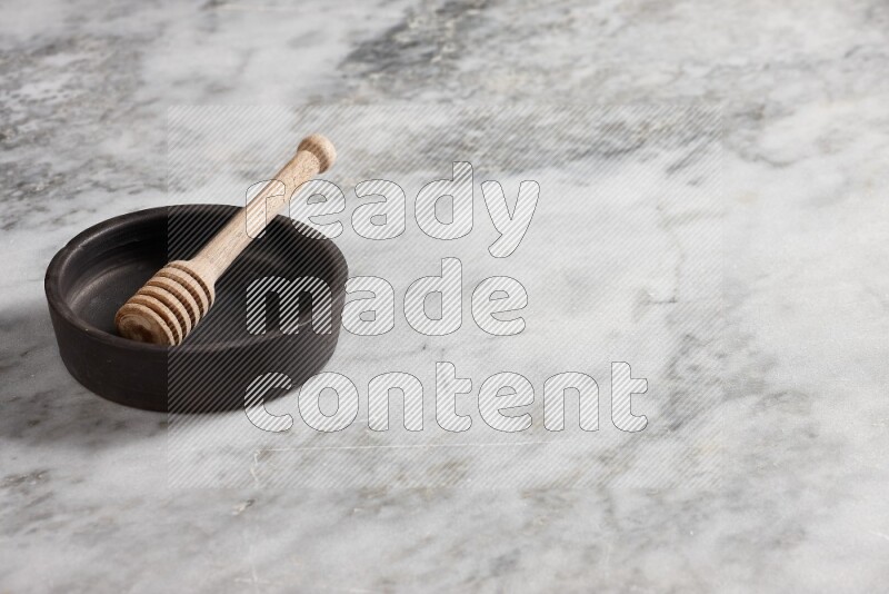 Black pottery oven plate with wooden honey dipper in it on grey marble background
