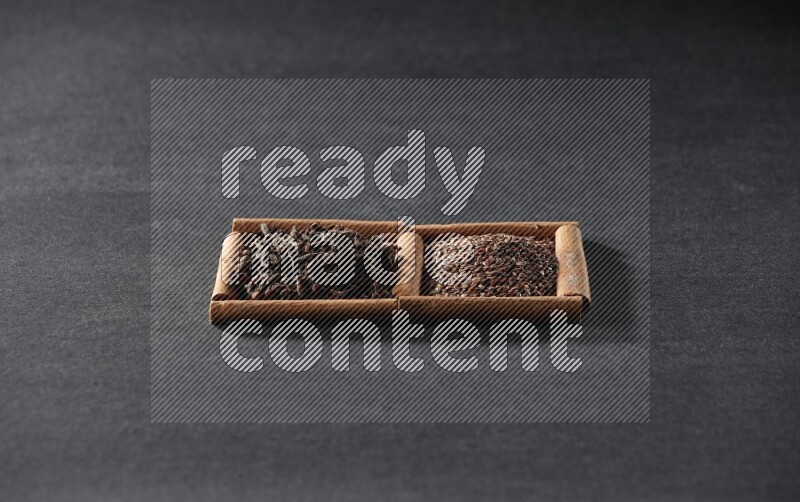 مربعان من أعواد القرفة ممتلئان ببذور الكتان والقرنفل علي خلفية سوداء