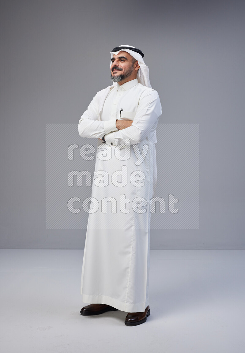 Saudi man Wearing Thob and white Shomag standing with crossed arms on Gray background