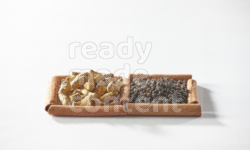 مربعان من أعواد القرفة ممتلئان بحبوب الفلفل الأسود وأصابع الكركم علي خلفية بيضاء