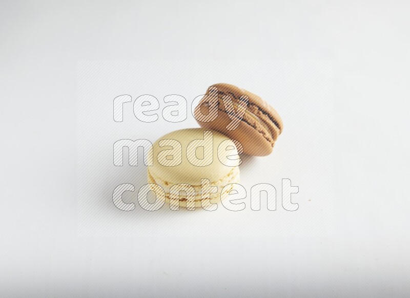 45º Shot of of two assorted Brown Irish Cream, and Yellow Vanilla macarons on white background