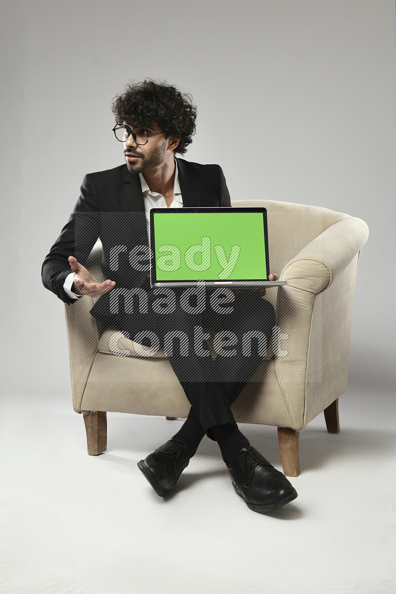 A man wearing formal sitting on a chair showing a laptop screen on white background
