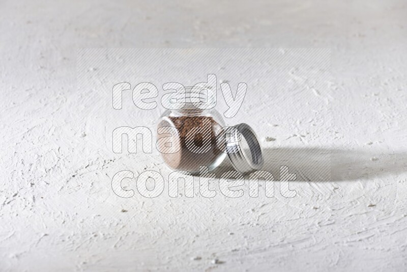 A glass spice jar full of cloves powder on textured white flooring