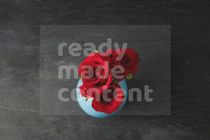 An arrangement of vivid red roses in a blue vase on black marble background