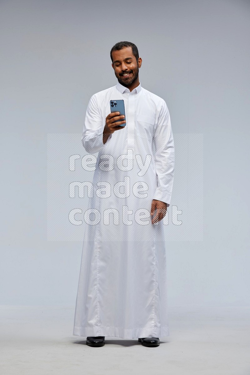 Saudi man wearing Thob standing texting on phone on Gray background