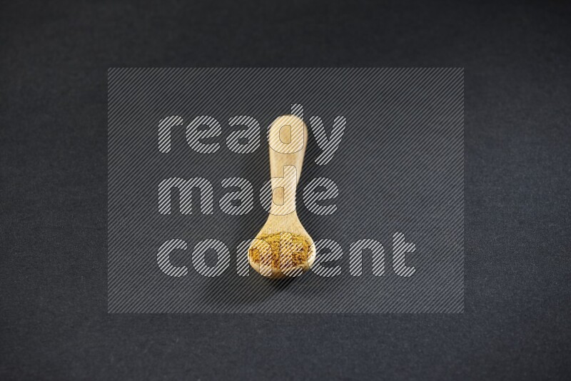 A wooden spoon full of turmeric powder on black flooring