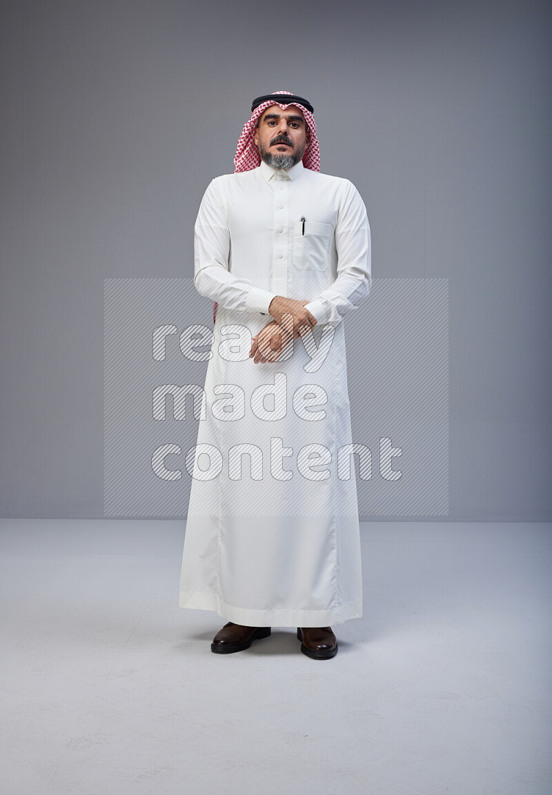 Saudi man Wearing Thob and red white Shomag standing interacting with the camera on Gray background