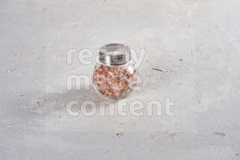 A glass jar full of coarse himalayan salt crystals on white background