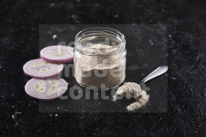 A glass jar full of onion powder on black background