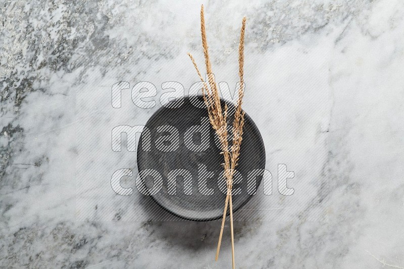 Wheat stalks on Black Pottery Plate on grey marble flooring, Top view