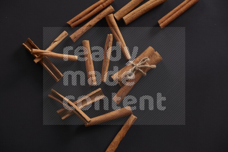 4 Cinnamon sticks stacked and bounded with more sticks in the background on black flooring