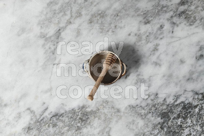 Multicolored Pottery Bowl with wooden honey handle in it, on grey marble flooring, Top View