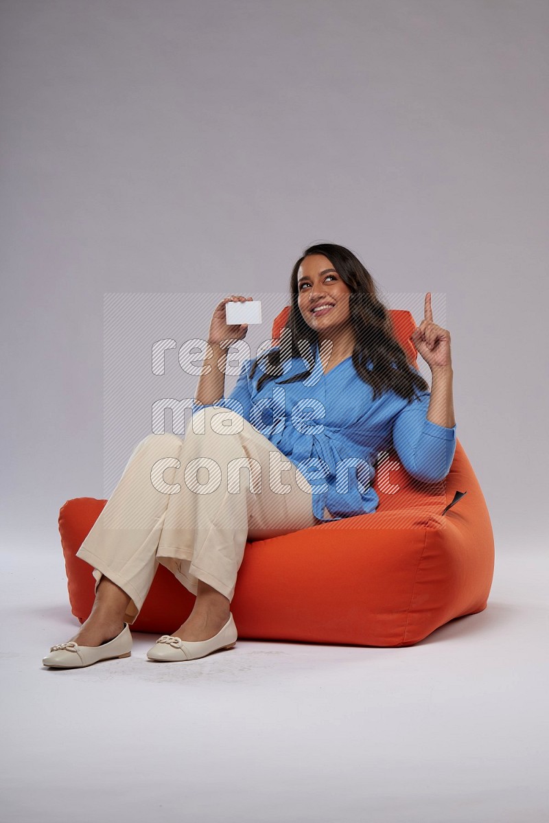 A woman sitting on an orange beanbag and holding ATM card