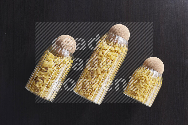Raw pasta in glass jars on black background