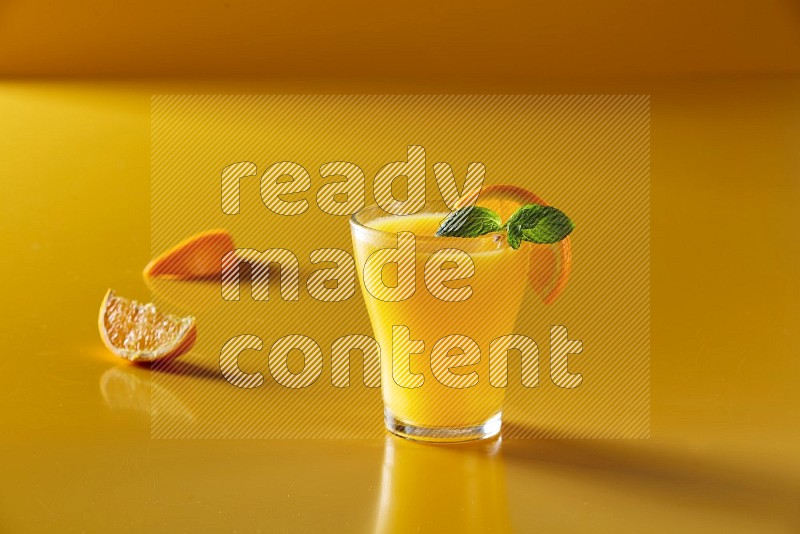 glass of orange juice with orange & mint  on yellow background
