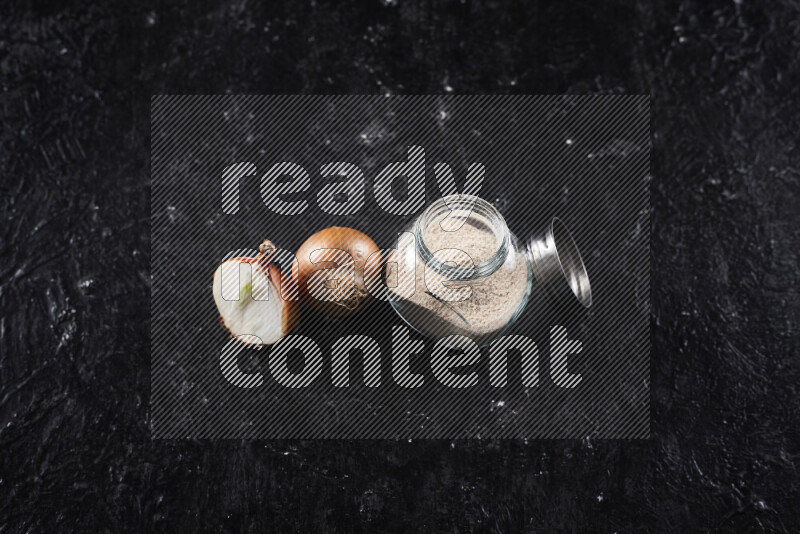 A glass jar full of onion powder on black background