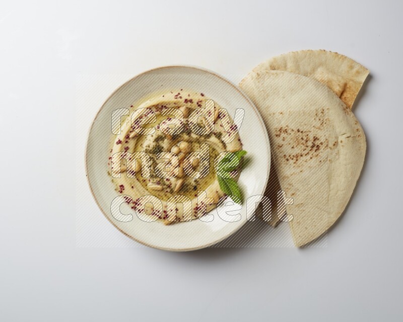 Hummus in a pottry plate garnished with zaatr & sumak on a white background