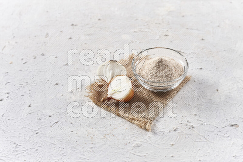 A glass bowl full of onion powder on burlap fabric on white background