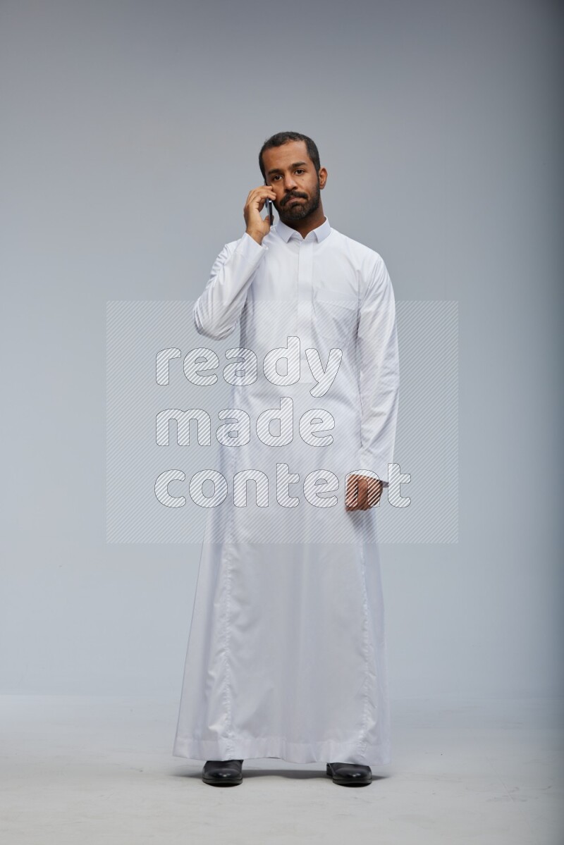 Saudi man wearing Thob standing talking on phone on Gray background