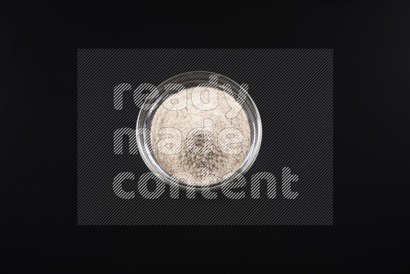 A glass bowl full of onion powder on black background